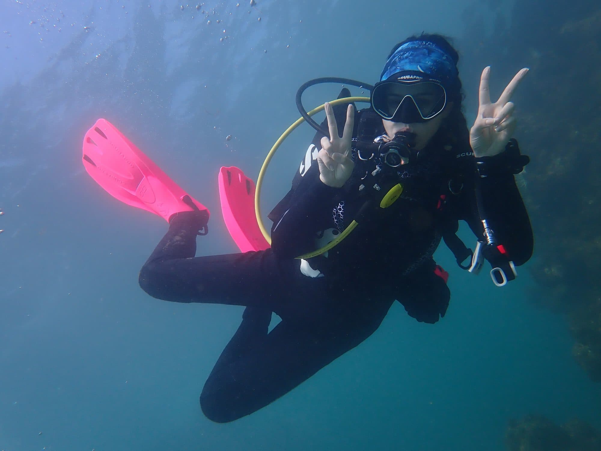 Diver with pink fins giving peace signs underwater
